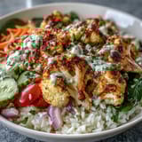 A colorful vegetarian bowl featuring spiced roasted cauliflower over basmati rice with fresh veggies and tangy lemon-tahini drizzle.