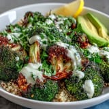 A close-up view shows crispy roasted broccoli florets and sliced avocado in a Roasted Broccoli Bowl, ready to be mixed with savory grains and sesame seeds.  