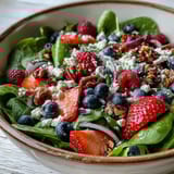 A vibrant Spinach and Berry Salad Bowl with fresh spinach leaves, sliced strawberries, blueberries, creamy goat cheese crumbles, and toasted walnuts tossed in a tangy bountiful vinaigrette.