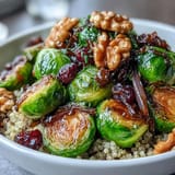 Hearty roasted Brussels sprouts and onion mixture paired with warm grains for a nourishing, gluten-free dinner bowl, garnished with crunchy nuts and seeds.