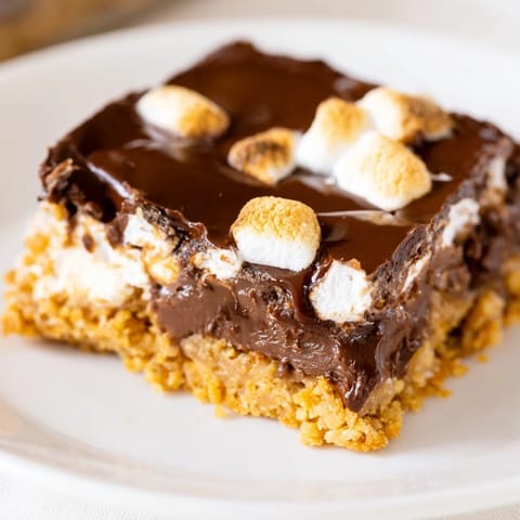 Golden toasted marshmallows melt over a rich chocolate layer of S'mores Bars on a rustic wooden board.