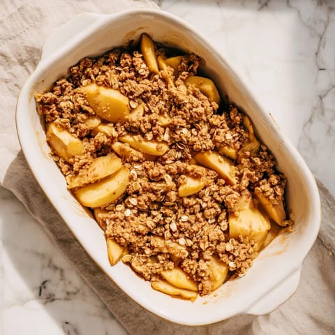 A scoop of vanilla ice cream melting over freshly baked Apple Crumble, bubbling apples and crunchy golden crumble topping.