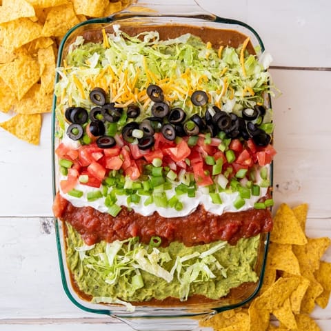 Homemade Seven-Layer Dip showing vibrant guacamole and chunky salsa, a chilled Tex-Mex appetizer ready for a party.