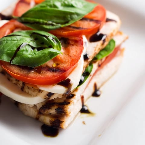 Fresh basil leaves and colorful tomatoes pair with tender grilled chicken in a simple, classic Chicken Caprese Salad presentation.