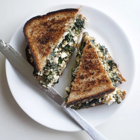 Close-up of a warm Feta & Spinach Stuffed Grilled Cheese on a rustic plate, highlighting the gooey feta and spinach filling.  