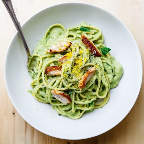 Creamy avocado chicken pasta served with grilled chicken slices and fresh basil garnish on a white plate.  