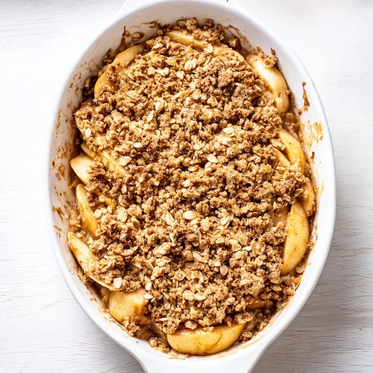 Homemade Apple Crumble in a baking dish with a spoon, cinnamon-dusted topping glistening, perfect for a cozy fall dessert.