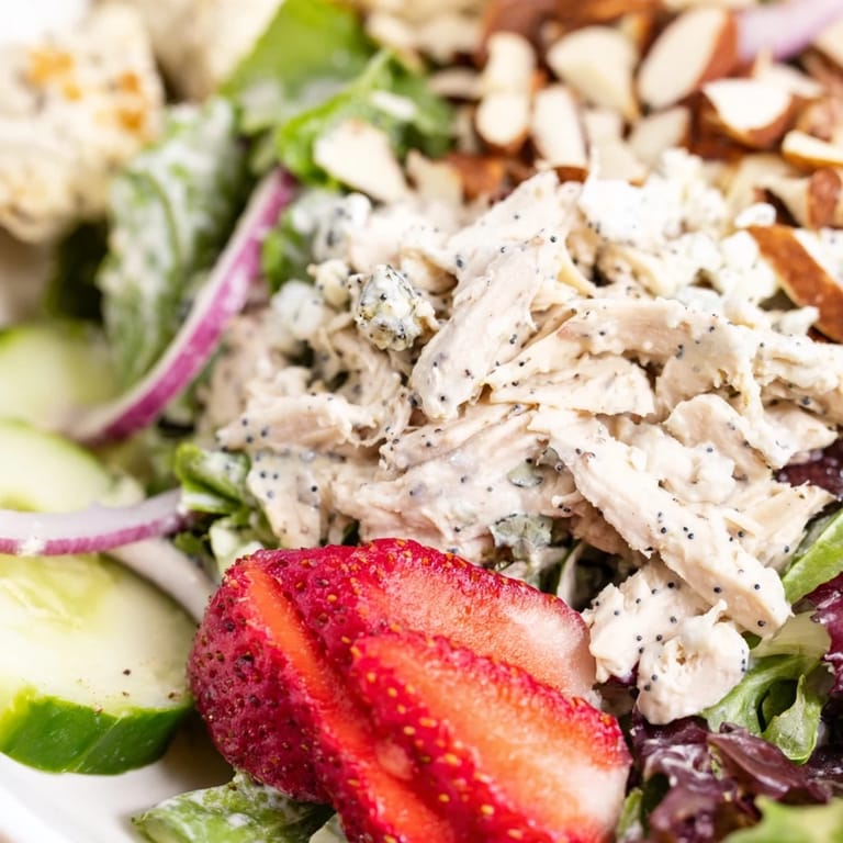 Strawberry Poppy Seed Chicken Salad served over mixed greens with feta, red onion, and toasted almonds for a refreshing lunch.