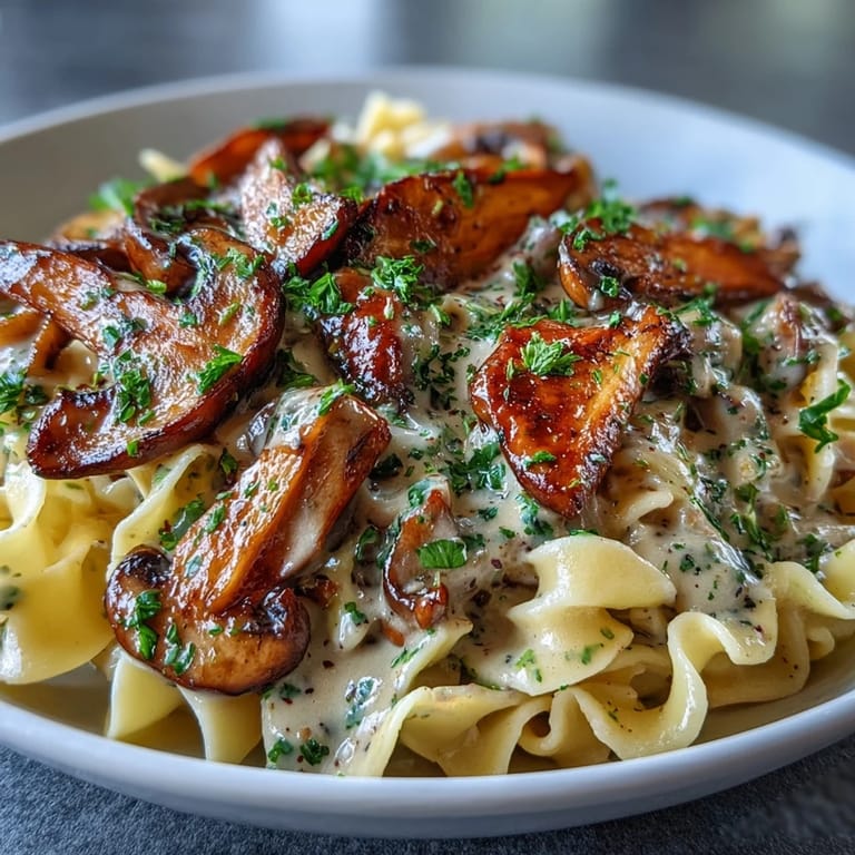A close-up of vegetarian Mushroom Stroganoff showing sautéed mushrooms and a velvety miso-infused sauce over pasta, ready to serve hot.
