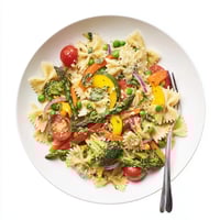 A close-up of vibrant Rainbow Veggie Pasta Primavera in a white bowl, featuring colorful vegetables and fresh herbs.